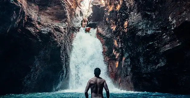 Un uomo in piedi nell'acqua davanti a una cascata.