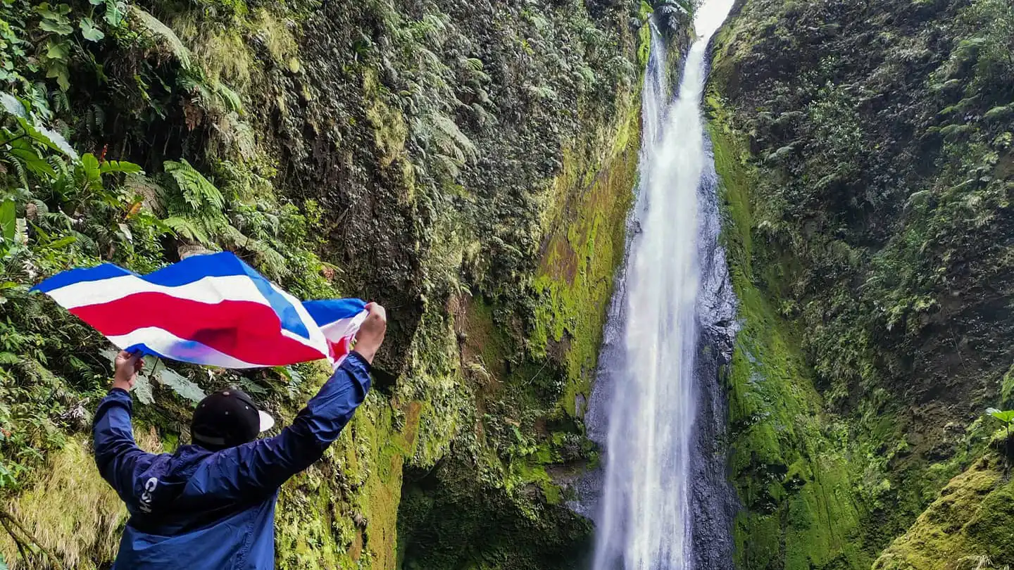 Un uomo che tiene una bandiera davanti a una cascata.