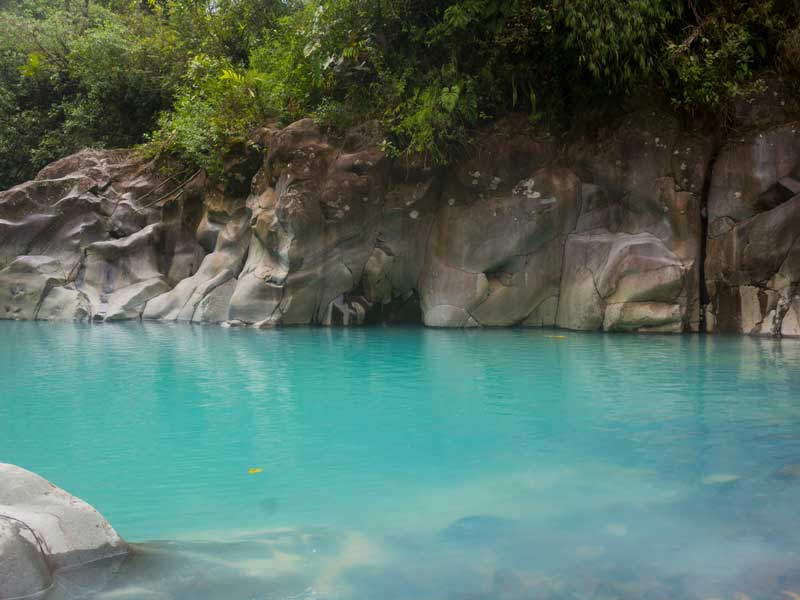 Una piscina di acqua blu circondata da rocce e alberi.