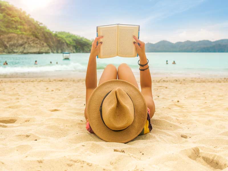 Una donna sdraiata sulla spiaggia che legge un libro.