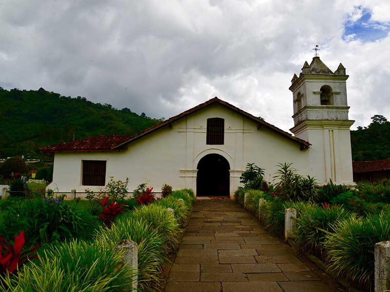 Una chiesa bianca con un campanile circondato dal verde.