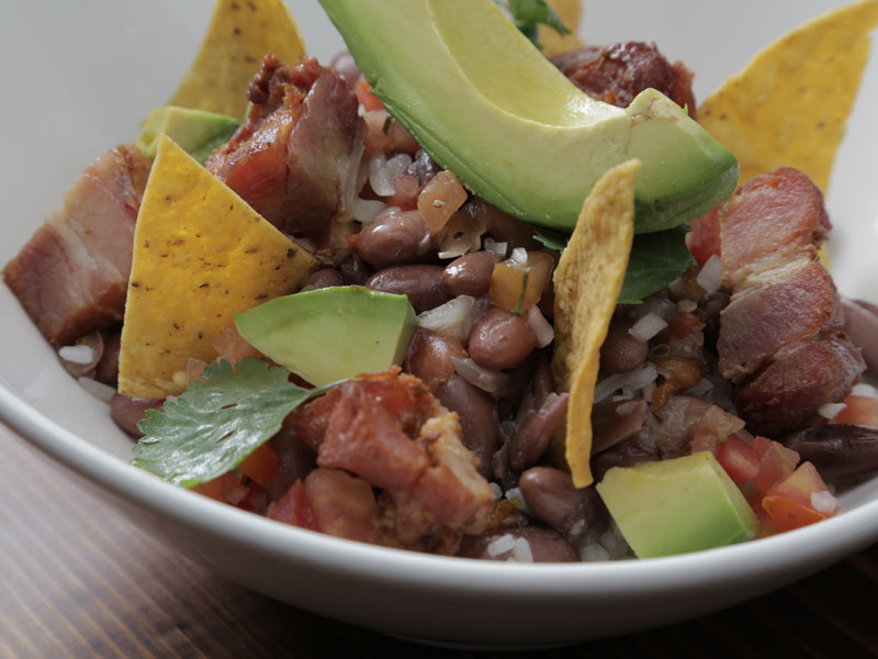 Una ciotola bianca riempita di fagioli, carne e avocado.