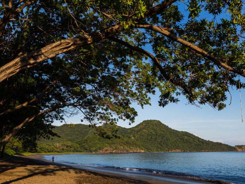Una persona che cammina su una spiaggia vicino a uno specchio d'acqua.