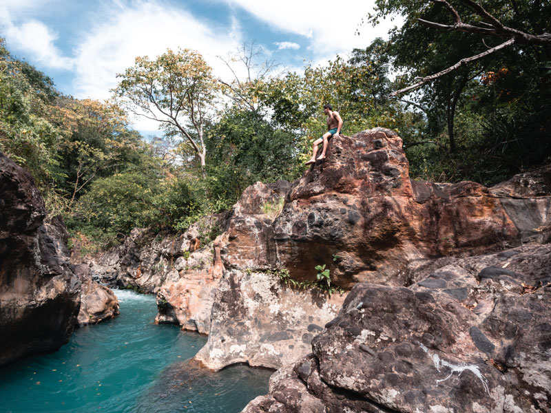 Una persona seduta su una roccia sopra un fiume.