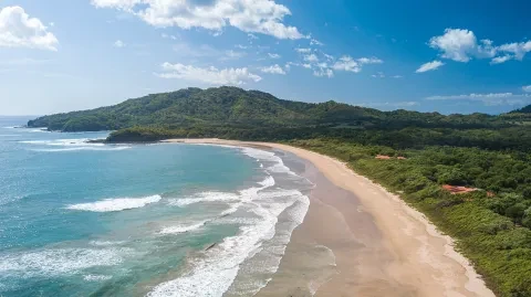 Vista aerea di una spiaggia sabbiosa lungo la costa pacific Costa Rica, circondata da acque turchesi e da rigogliose colline verdeggianti.