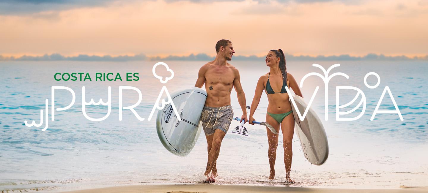 Coppia che cammina sulla spiaggia con tavole da surf e testopura vida" intorno a loro