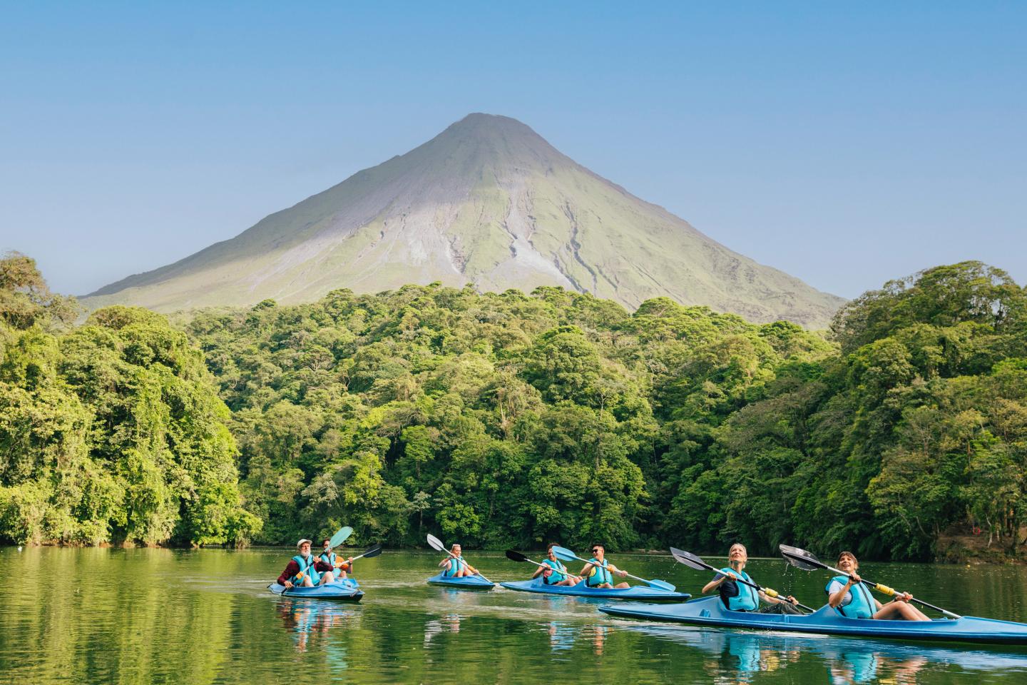 Escursione in kayak di gruppo su un lago tranquillo circondato dalla foresta pluviale, con il vulcano Arenal che si erge sullo sfondo.