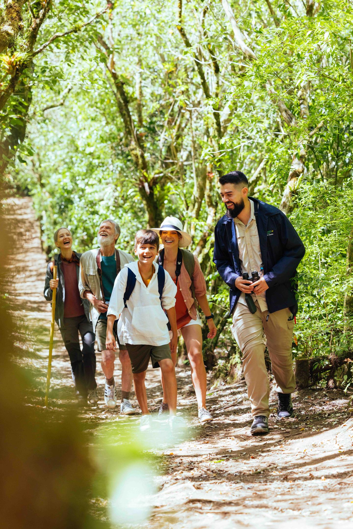 Un piccolo gruppo di escursionisti cammina lungo un sentiero ombreggiato nel bosco, accompagnato da una guida.